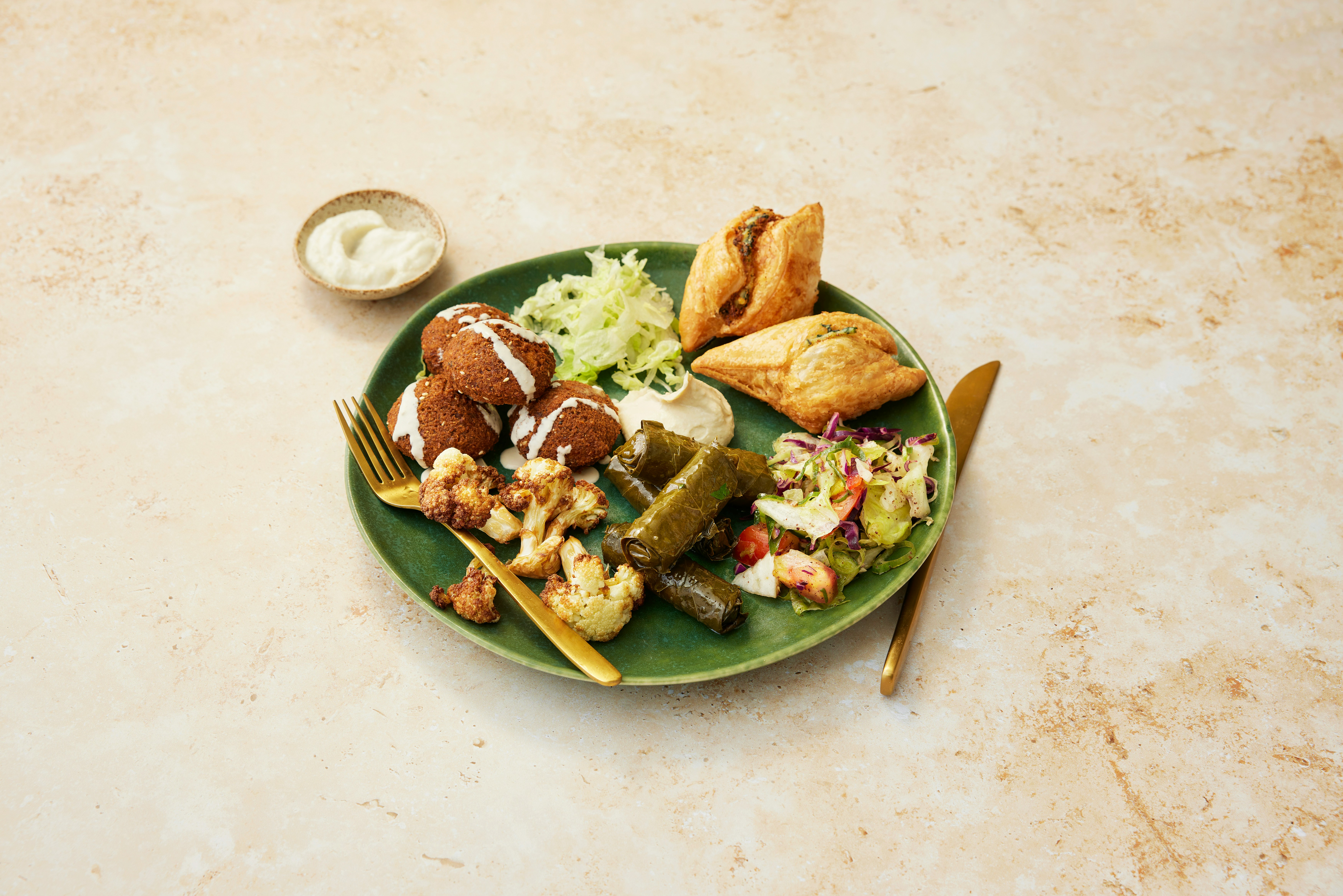 A green plate of falafel, dolmades, roasted cauliflower, and sambousek pastries — typical Amman mezze
