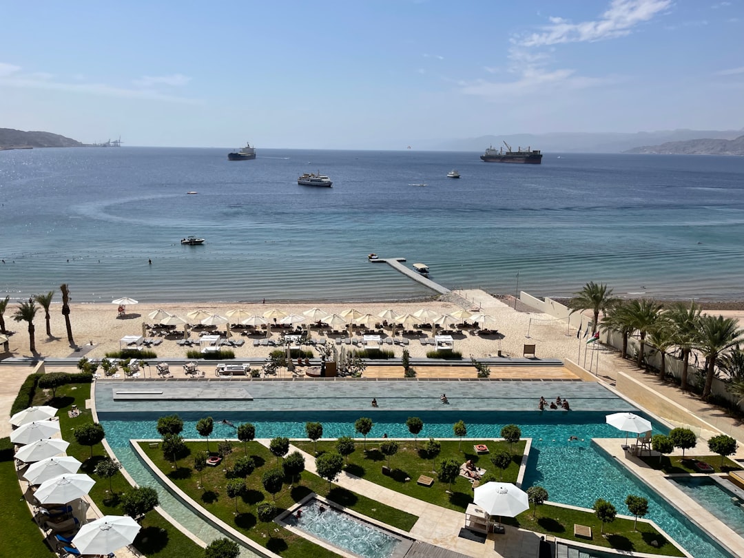Aerial view of an Aqaba beachfront resort with a long pool, sunbeds, and the calm blue waters of the Red Sea stretching toward distant mountains