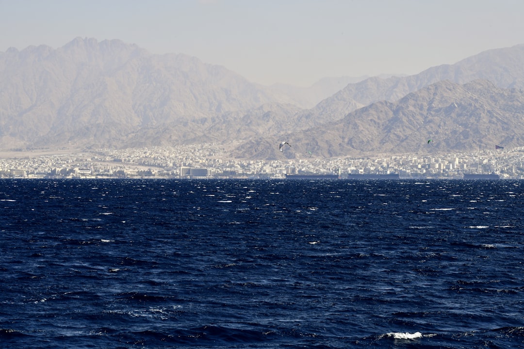 View of Aqaba city from across the Red Sea, with low-rise buildings stretching along the Jordanian shoreline and arid mountains rising behind
