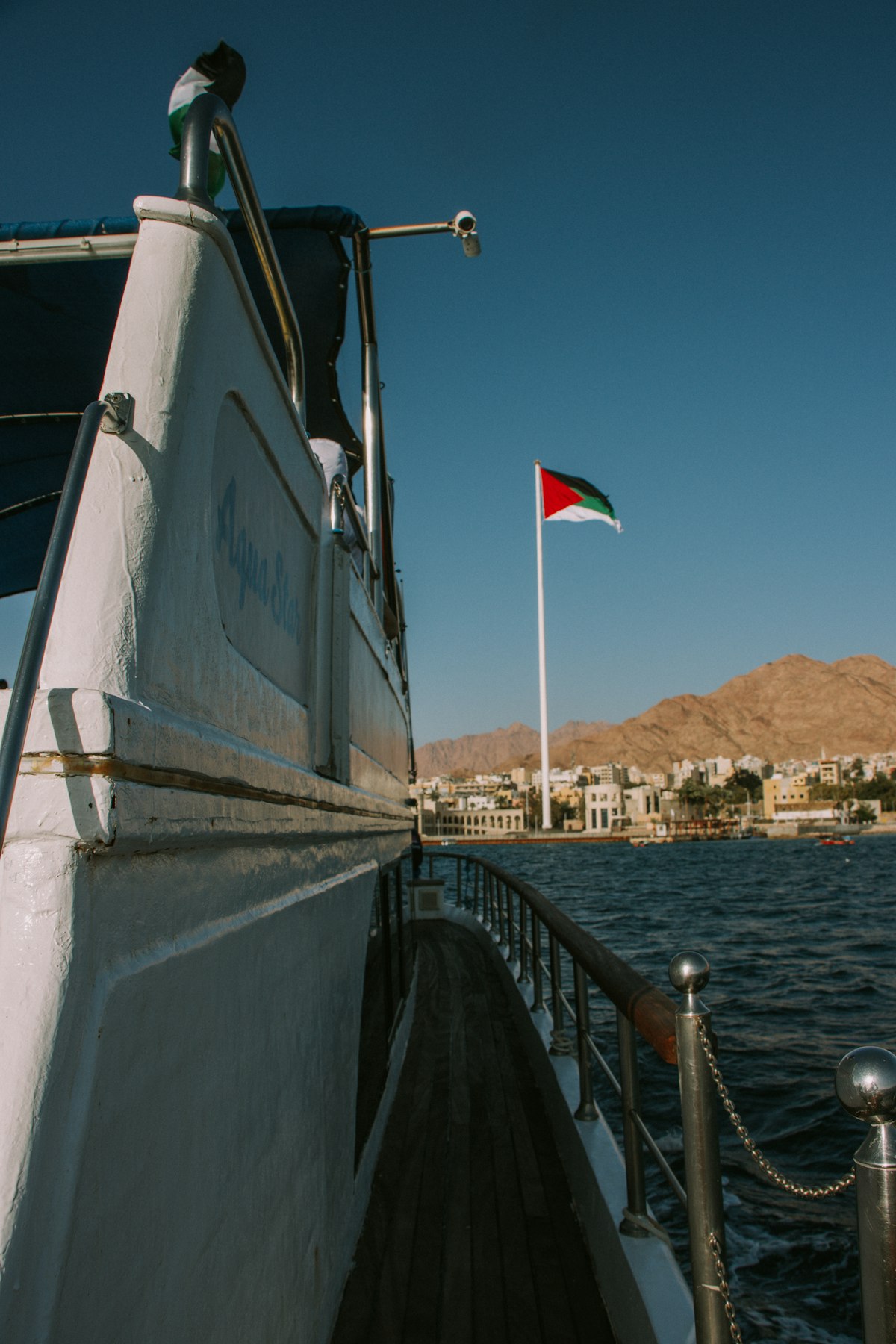 View from a boat deck in Aqaba marina with the Jordanian flag flying above the Red Sea coastline