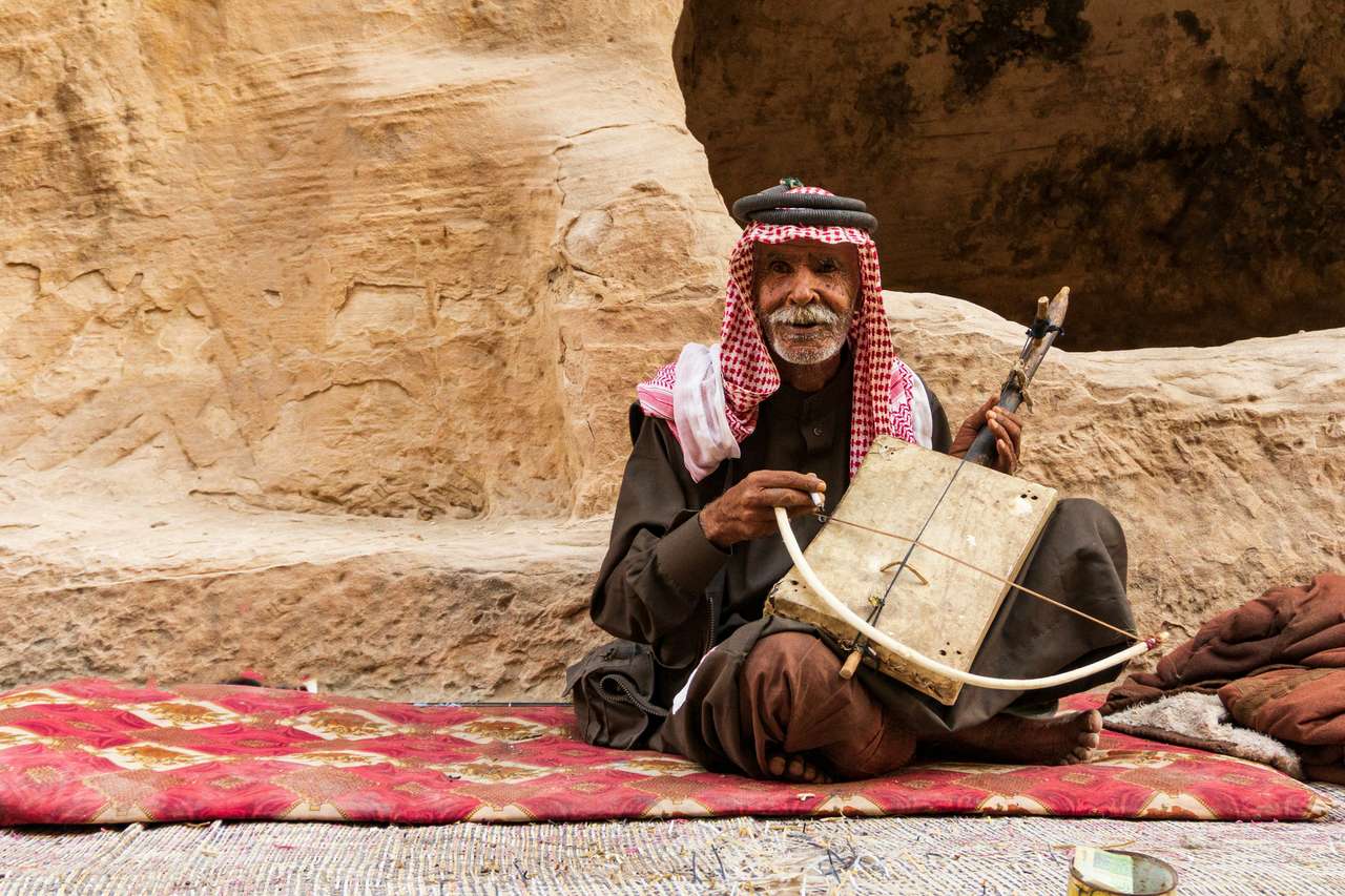 Elderly Bedouin man playing a rababa fiddle in a sandstone cave at Little Petra, Jordan