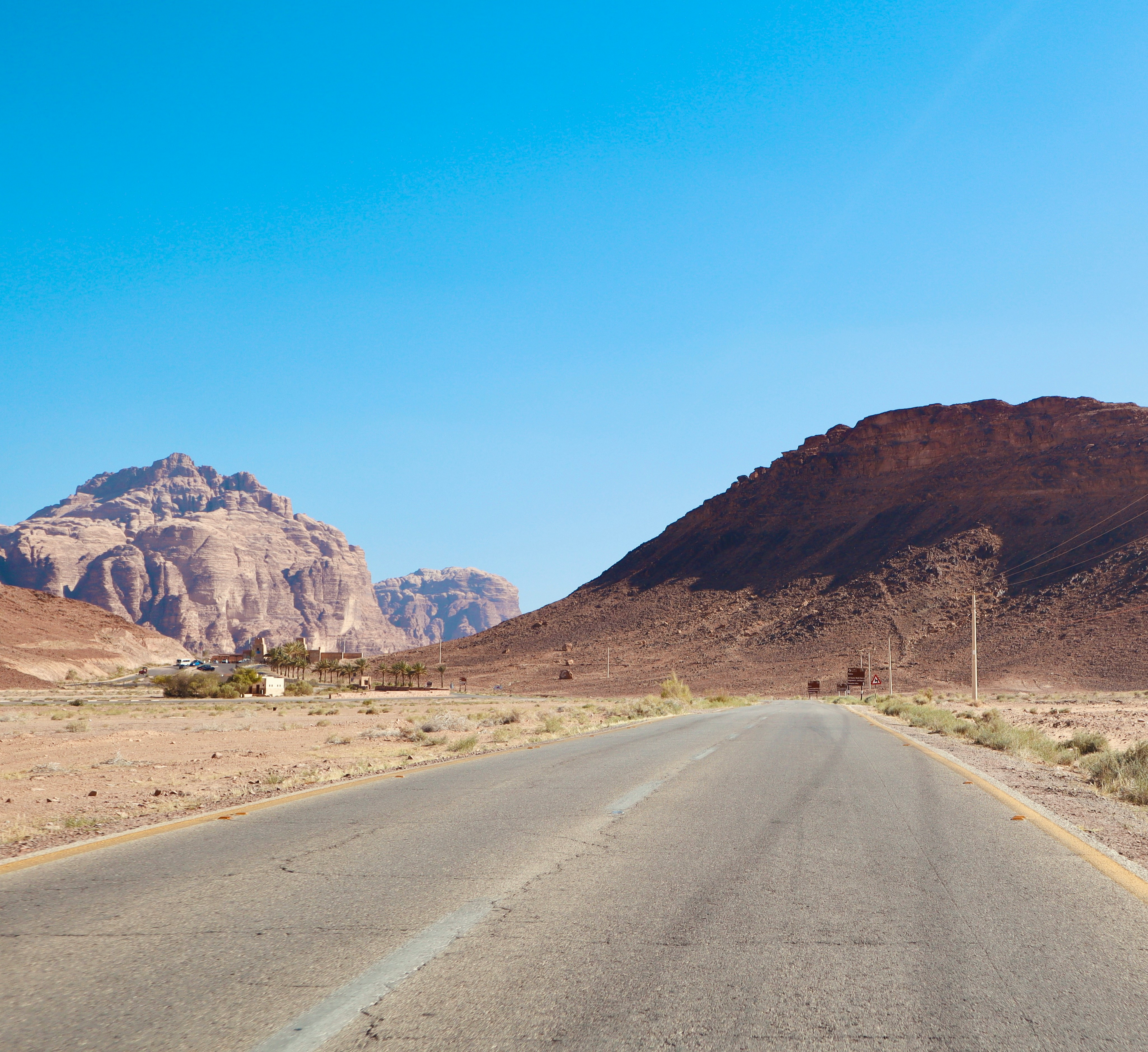 Open desert road cutting through Wadi Rum with red sandstone mountains on either side under a clear blue sky
