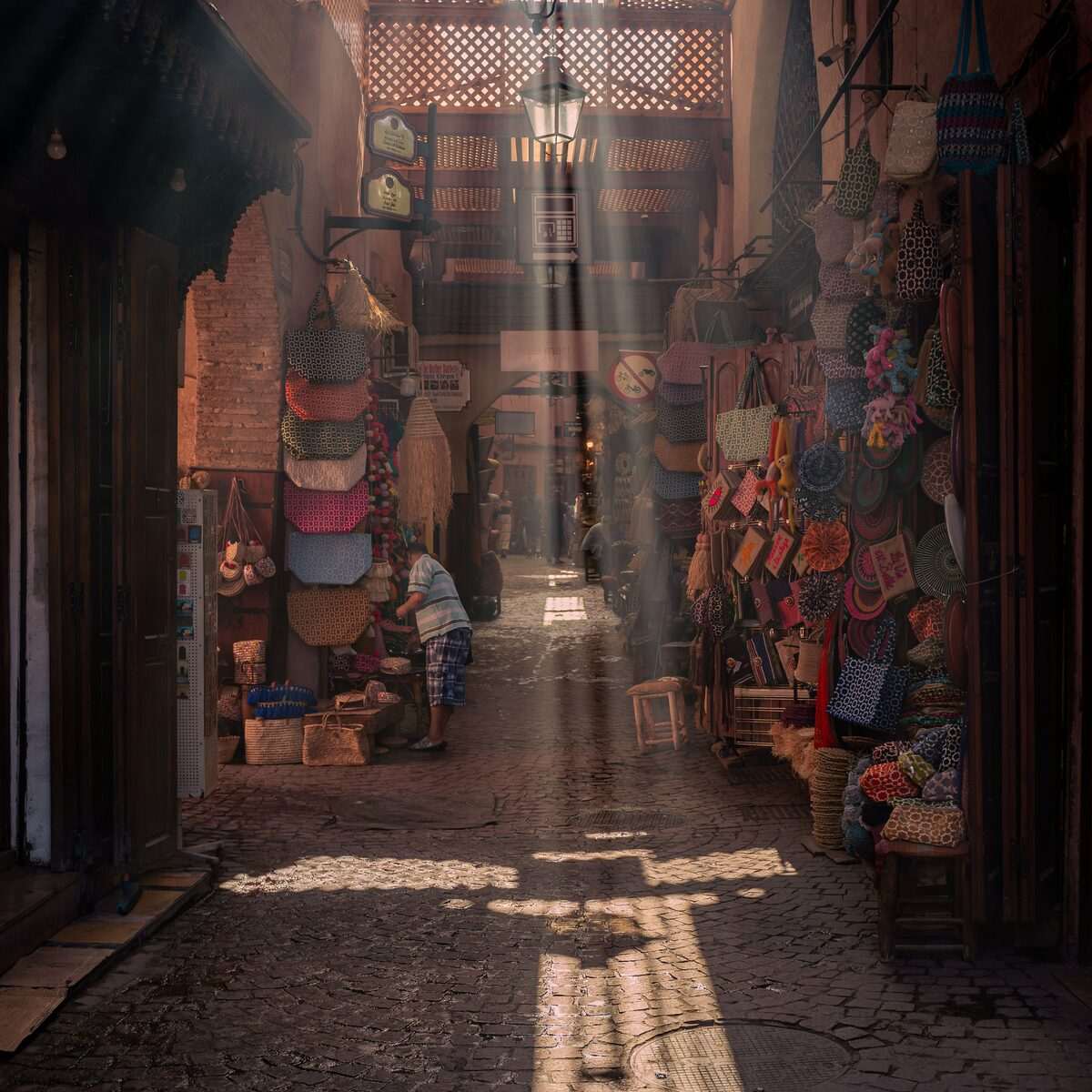 Sunlit alleyway in Marrakech medina with colourful market stalls and lanterns, Morocco
