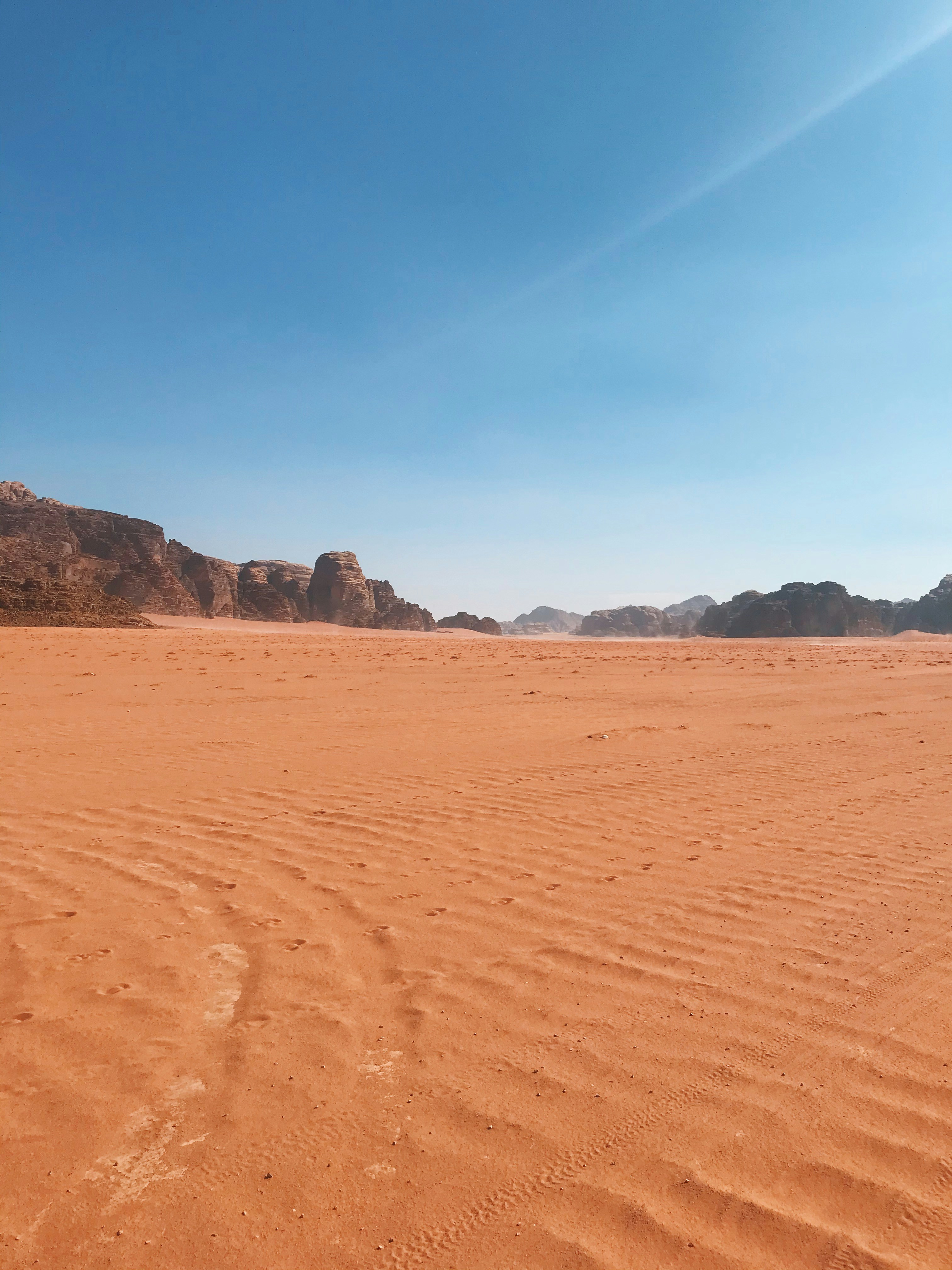 Vast red sand plain stretching toward sandstone mountains in Wadi Rum, Jordan