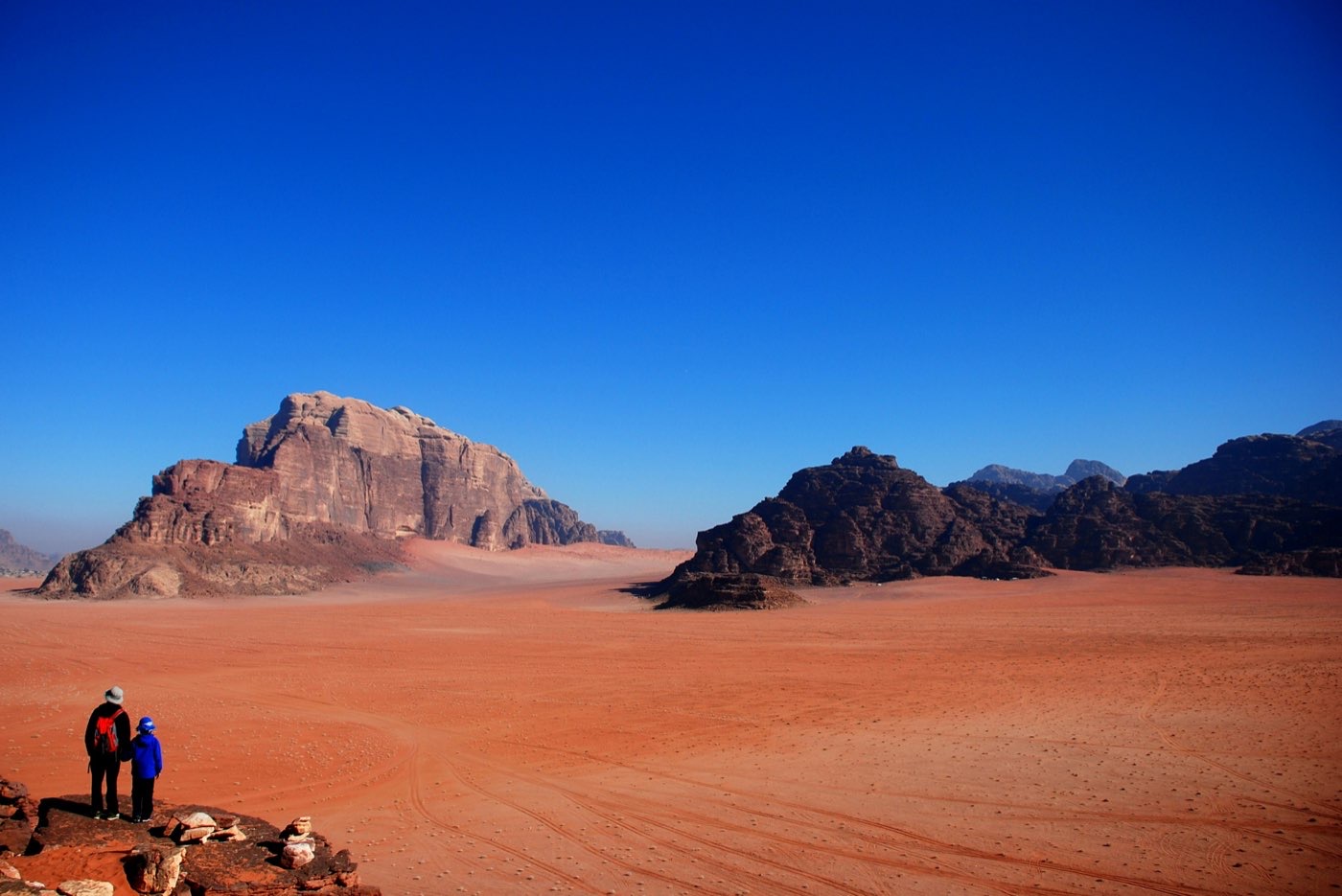 Two visitors look out over the vast red sand plains and rock formations of Wadi Rum, Jordan