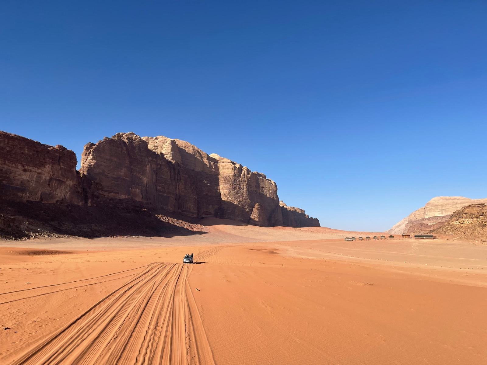 A 4x4 jeep crossing the red sands of Wadi Rum desert beneath sandstone cliffs, Jordan