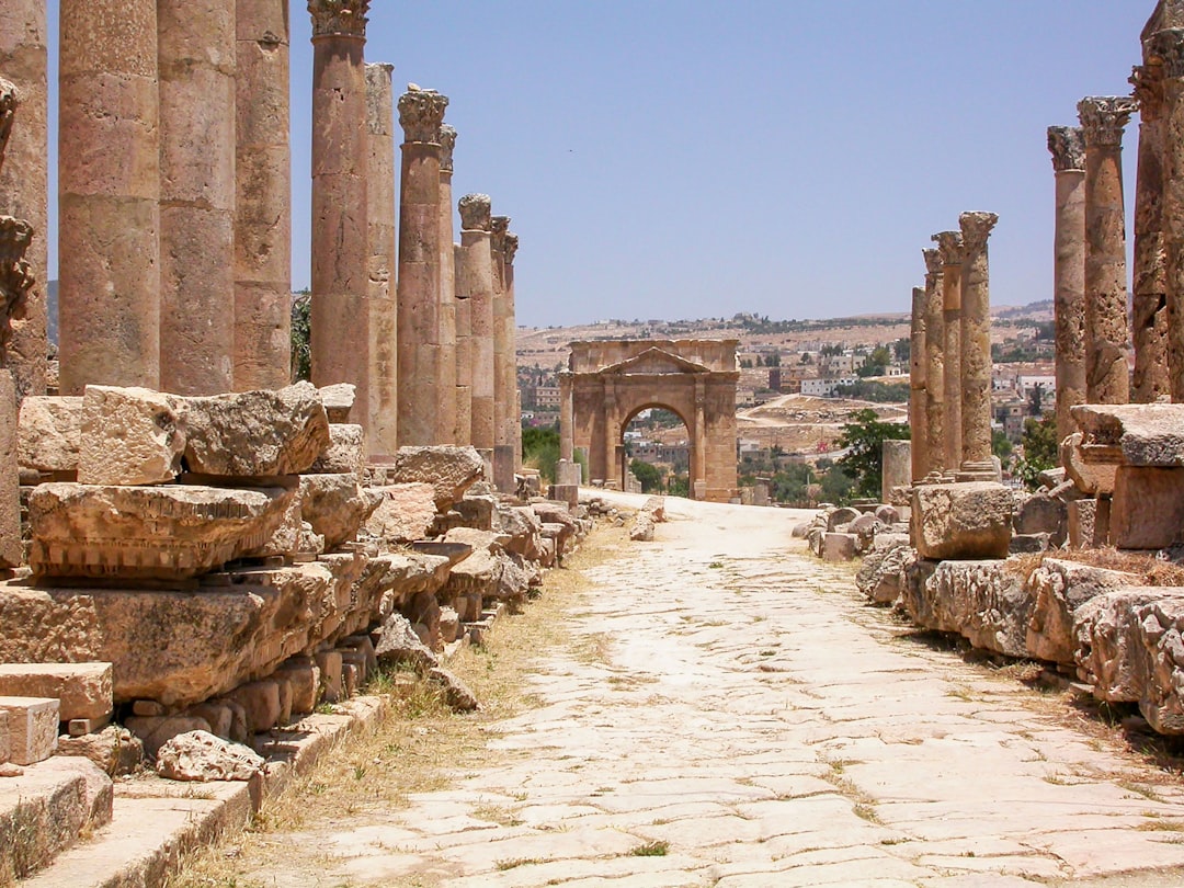 Cardo Maximus colonnaded street at Jerash, Jordan, with tall Roman columns lining a stone-paved road and a triumphal arch in the distance