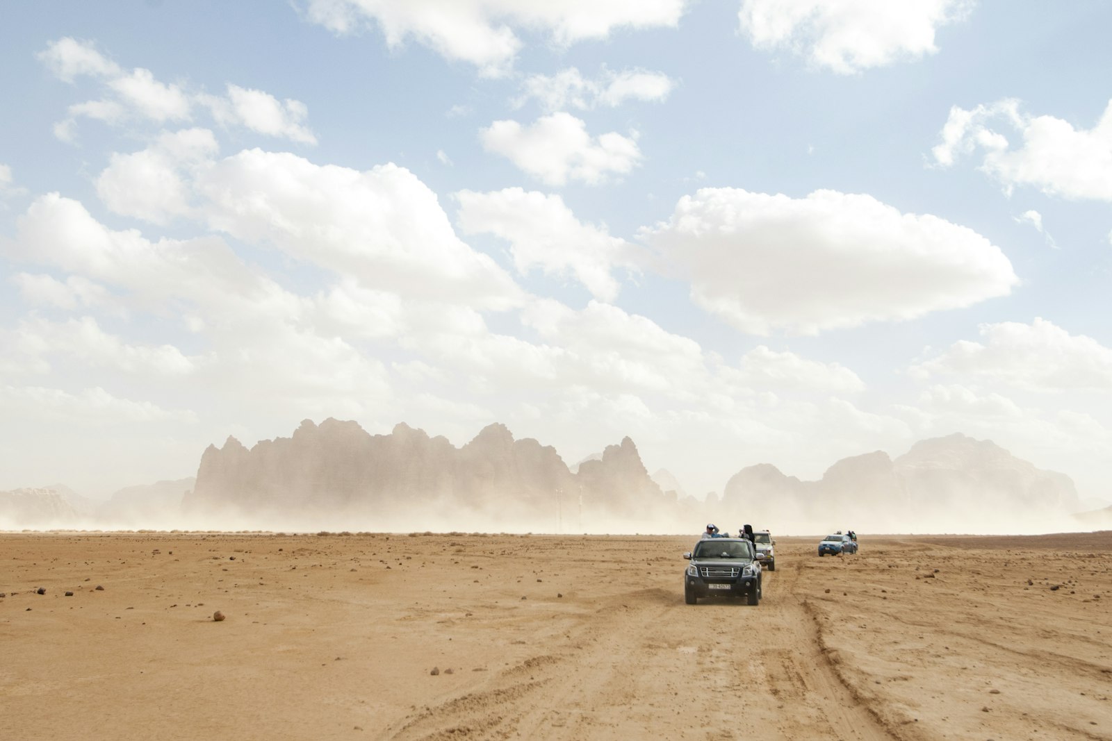 Convoy of vehicles driving across Jordan's desert landscape with rocky mountains in the background