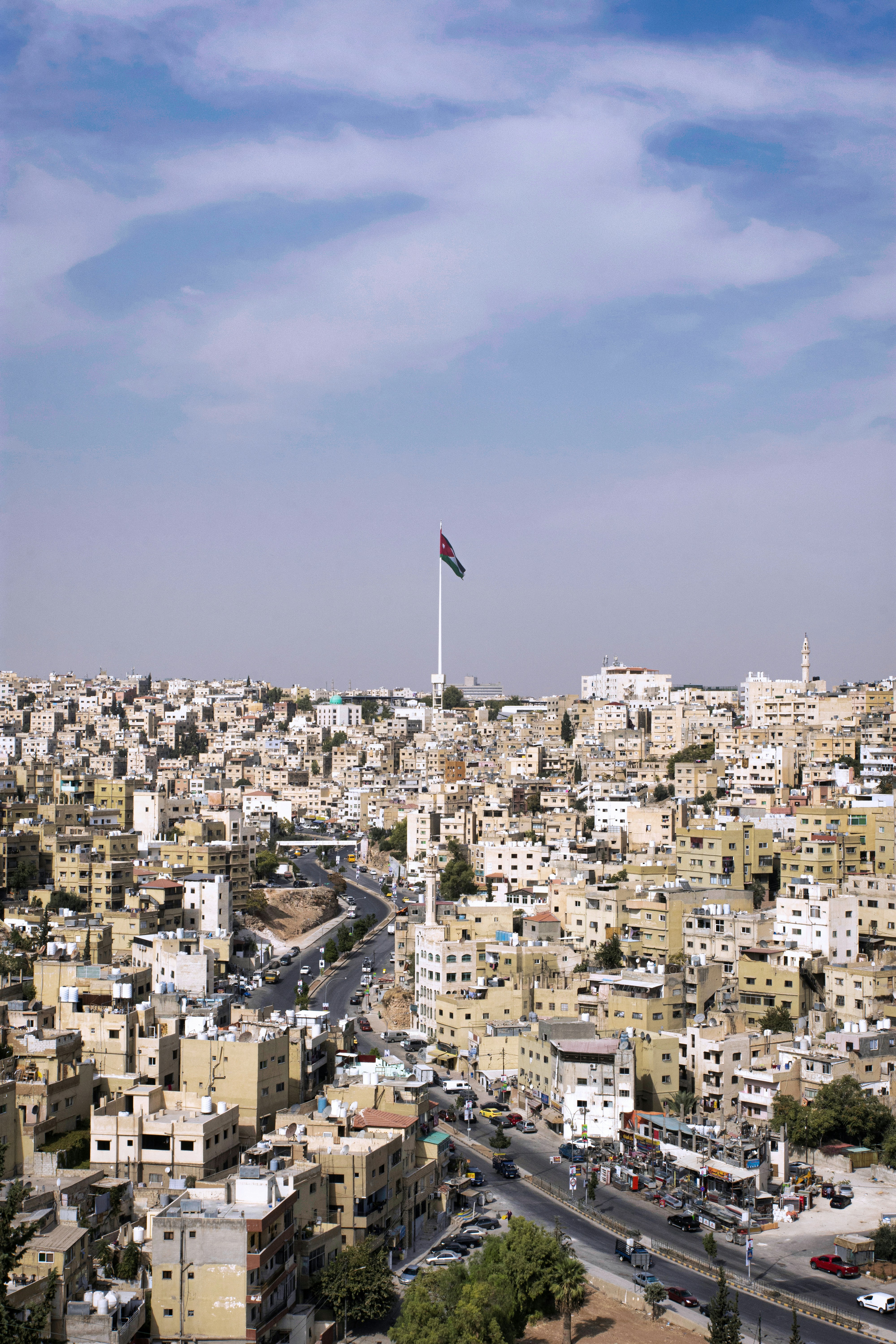View over Amman's white stone buildings with the Jordanian flag on a tall flagpole against a blue sky