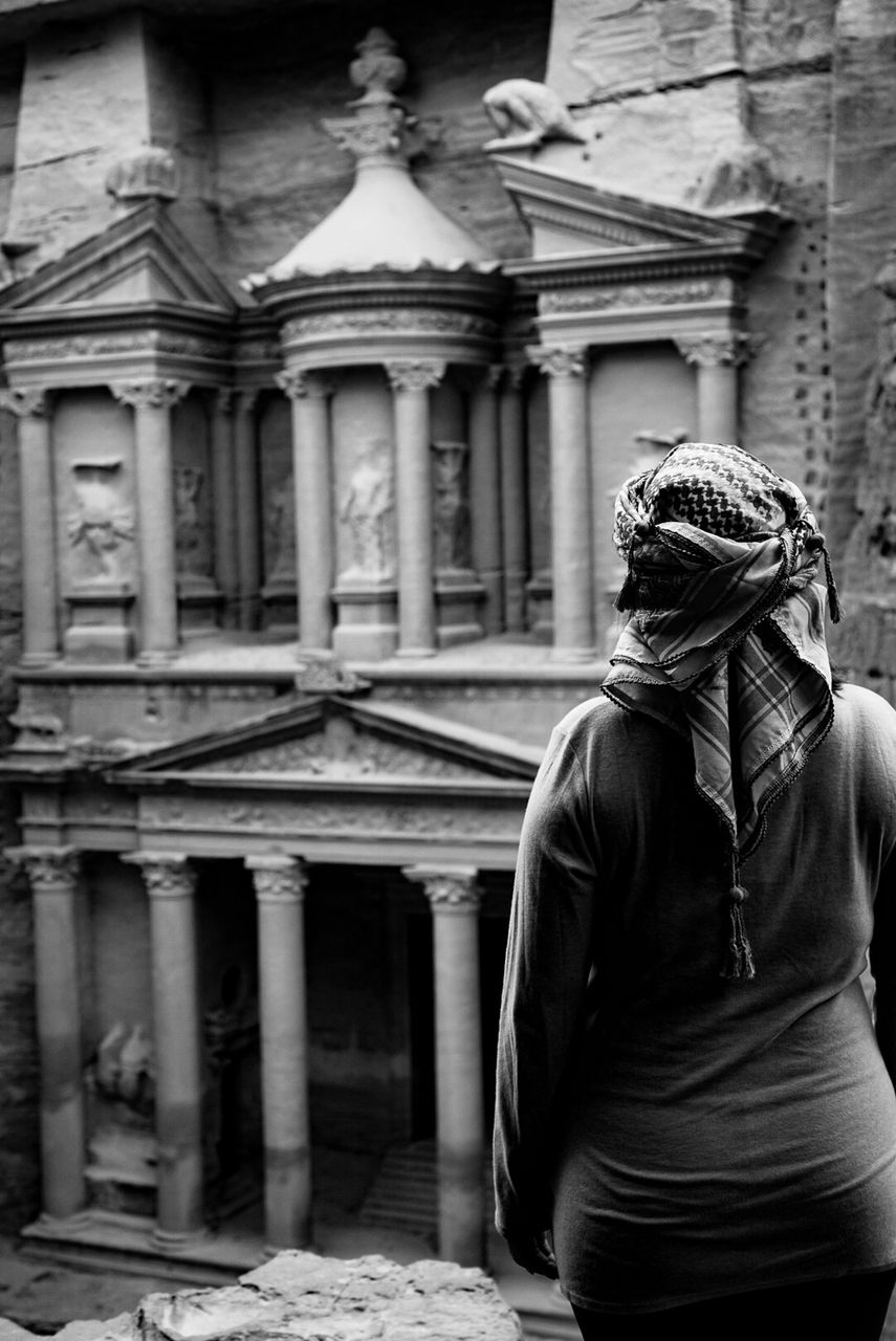 Traveler in keffiyeh headscarf stands before the carved sandstone facade of Petra's Treasury, Jordan