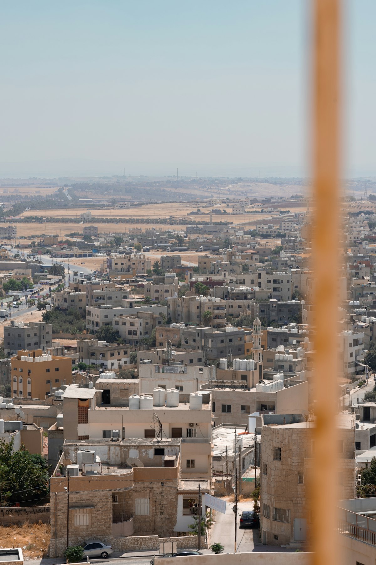 Elevated view over Madaba showing clusters of stone and concrete buildings stretching toward the desert plains, Jordan