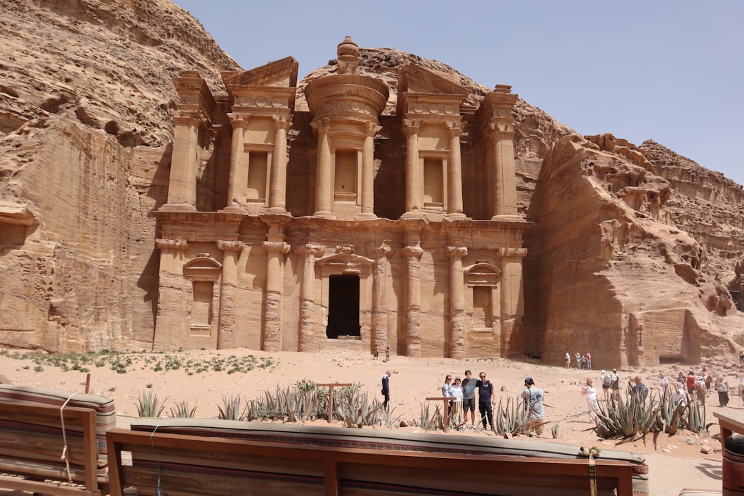 Visitors standing in front of the Monastery at Petra, Jordan, with the massive carved sandstone facade filling the frame