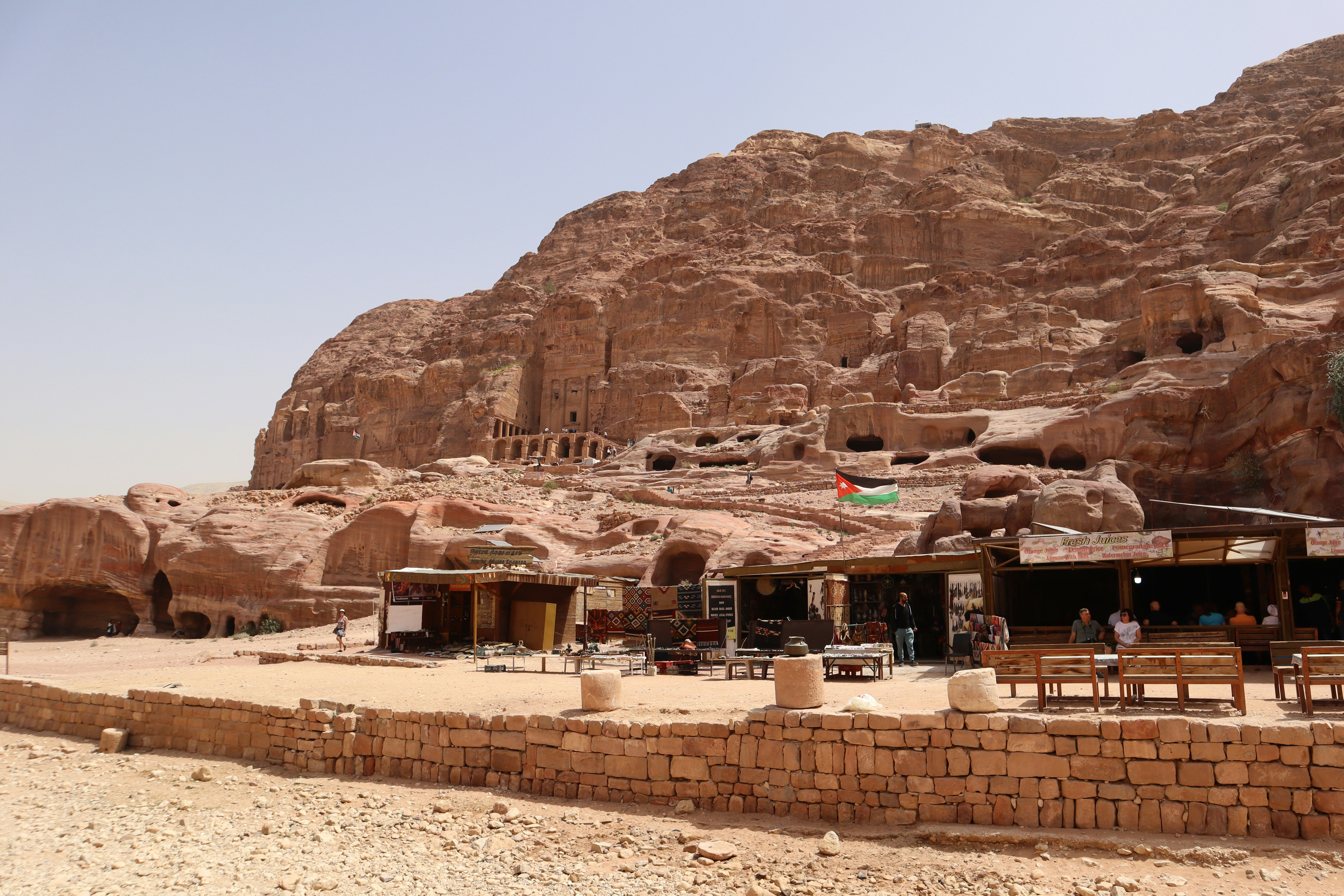 Outdoor dining area with wooden tables and benches set against the carved sandstone cliffs of Petra, Jordan