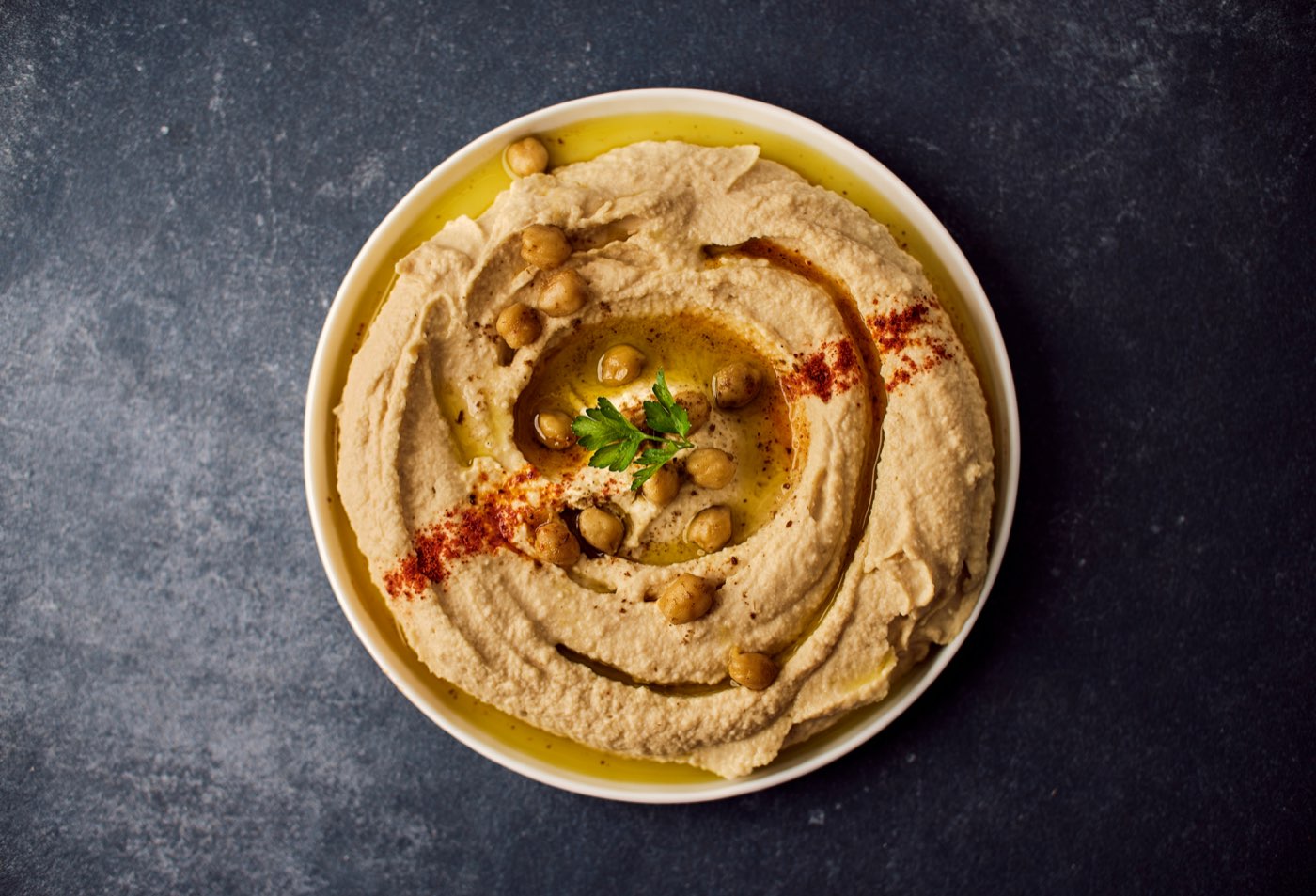 A smooth bowl of hummus with olive oil, chickpeas, and paprika — iconic vegan Jordanian food