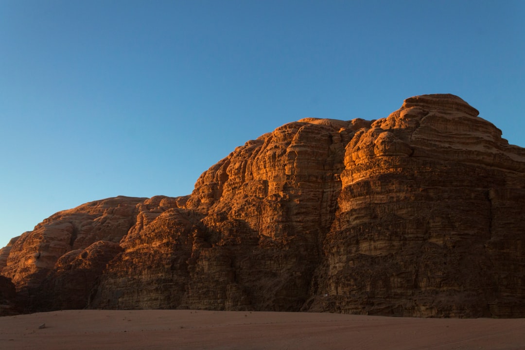 Layered red sandstone cliffs lit by the setting sun in Wadi Rum, Jordan, against a clear blue sky