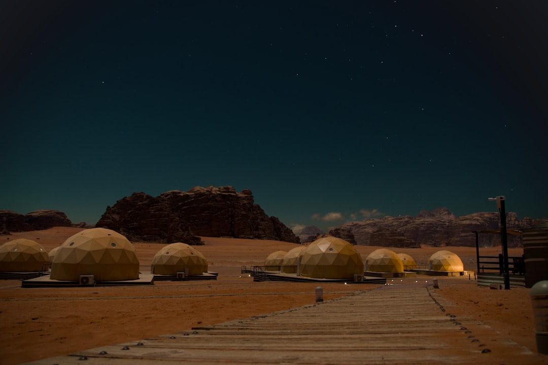Golden dome glamping tents lit at night at a Wadi Rum desert camp, with red sandstone mountains and a star-filled sky behind