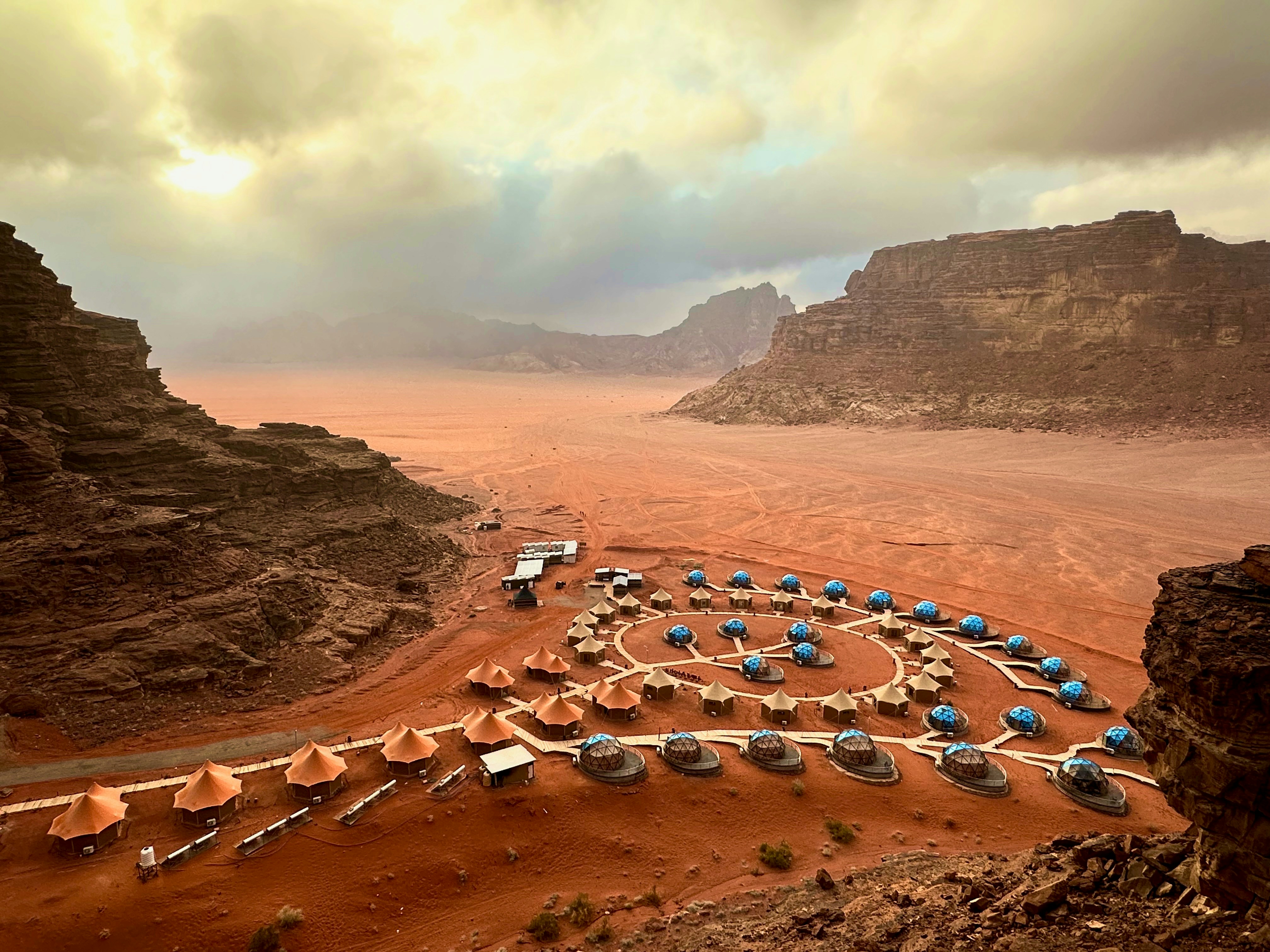 Aerial view of a desert camp with dome tents arranged in a circular layout among the red sand and rock formations of Wadi Rum, Jordan
